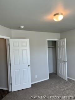 unfurnished bedroom with dark carpet and a closet