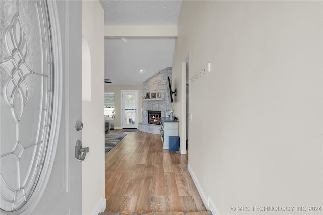 entrance foyer with light wood-type flooring, lofted ceiling, a textured ceiling, and a stone fireplace