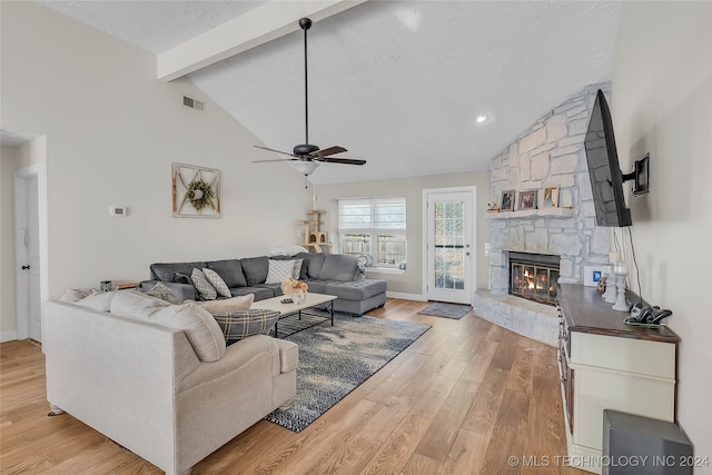 living room featuring light hardwood / wood-style floors, a textured ceiling, beam ceiling, a fireplace, and ceiling fan