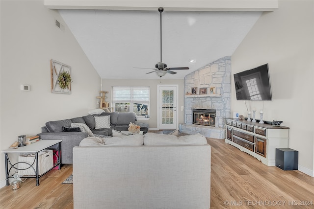 living room with light wood-type flooring, vaulted ceiling with beams, a stone fireplace, and ceiling fan