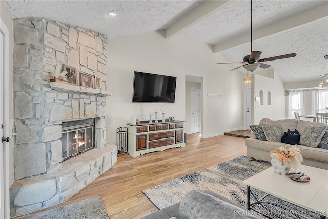 living room featuring a textured ceiling, vaulted ceiling with beams, a stone fireplace, and hardwood / wood-style floors