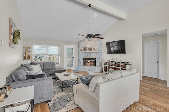 living room featuring ceiling fan, beam ceiling, a textured ceiling, a fireplace, and light wood-type flooring