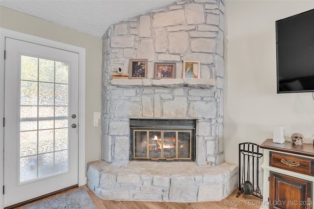 interior details featuring a textured ceiling, a stone fireplace, and hardwood / wood-style flooring