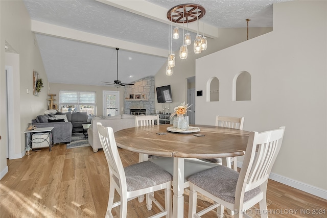 dining area featuring ceiling fan, vaulted ceiling with beams, a textured ceiling, a fireplace, and light hardwood / wood-style floors