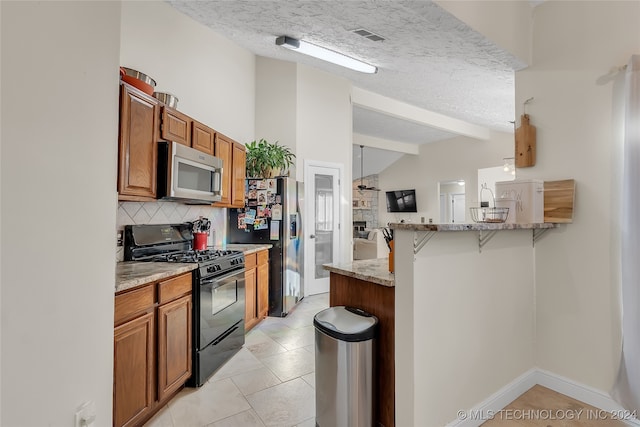 kitchen with a textured ceiling, light tile patterned flooring, kitchen peninsula, a kitchen breakfast bar, and stainless steel appliances