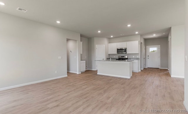 kitchen with light hardwood / wood-style floors, light stone counters, white cabinets, stainless steel appliances, and a kitchen island with sink