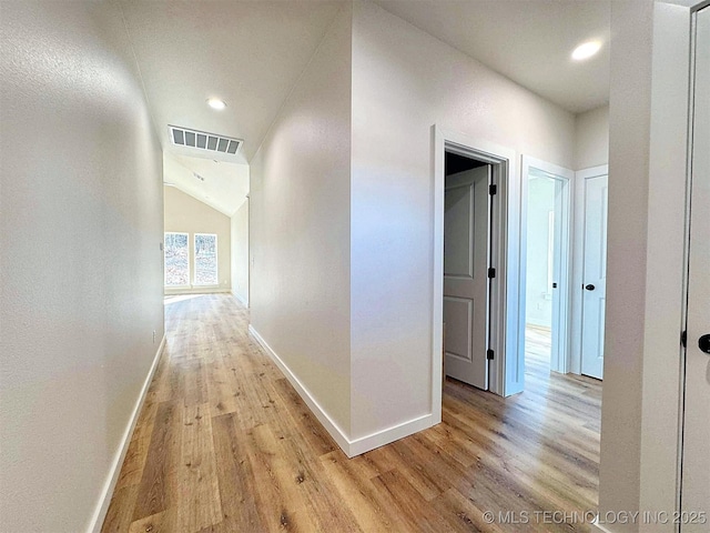 corridor featuring light wood finished floors, visible vents, baseboards, vaulted ceiling, and recessed lighting