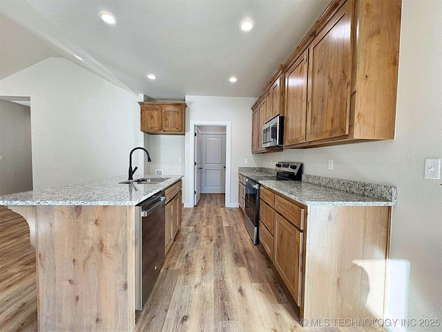 kitchen with brown cabinets, light wood finished floors, stainless steel appliances, a sink, and light stone countertops