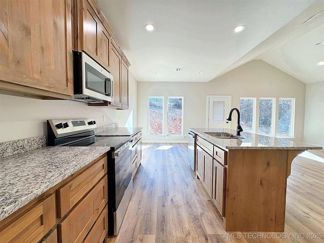 kitchen featuring light stone counters, a kitchen island with sink, a sink, appliances with stainless steel finishes, and light wood-type flooring