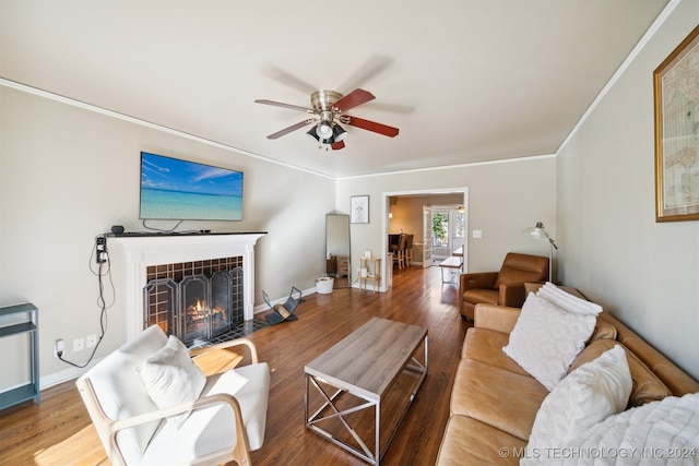 living room with ceiling fan, hardwood / wood-style flooring, a tiled fireplace, and crown molding