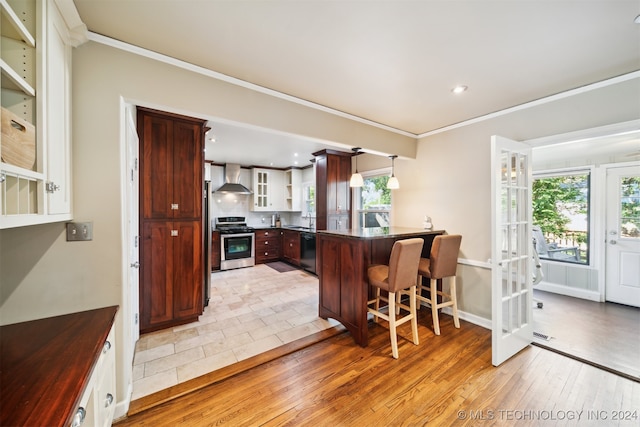 kitchen featuring pendant lighting, light hardwood / wood-style floors, stainless steel range oven, wall chimney range hood, and a kitchen breakfast bar