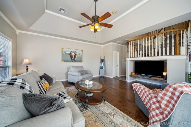 living room with a raised ceiling, crown molding, ceiling fan, and dark wood-type flooring