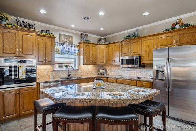 kitchen with sink, a center island, stainless steel appliances, a breakfast bar, and crown molding