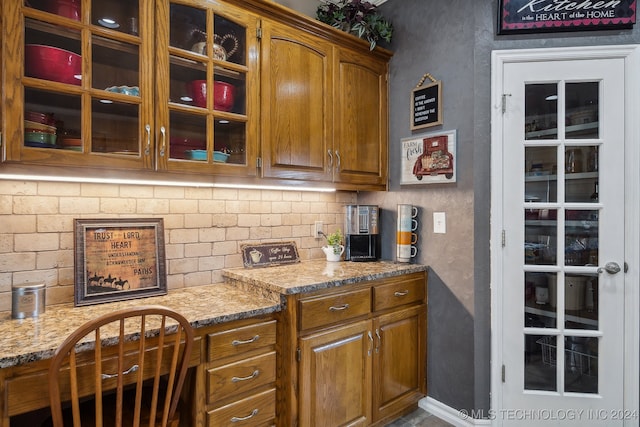 3691 E 390th Rd, Oologah, OK 74053 - kitchen with backsplash, brown cabinetry, glass insert cabinets, light stone counters, and a textured wall