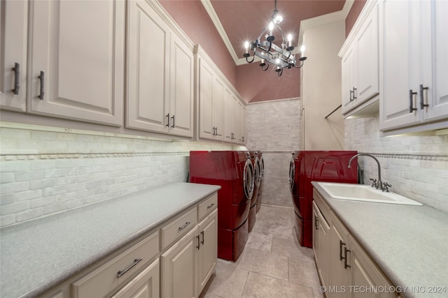 laundry area with ornamental molding, sink, cabinets, independent washer and dryer, and a notable chandelier