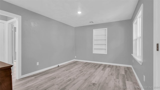 unfurnished room featuring built in shelves and light hardwood / wood-style flooring