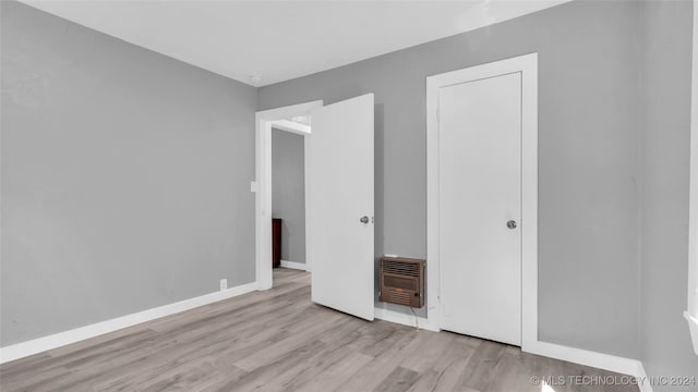 unfurnished bedroom with heating unit, a closet, and light hardwood / wood-style flooring