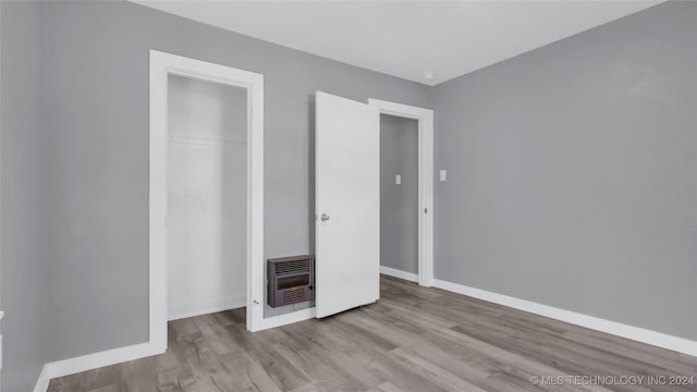 unfurnished bedroom featuring a closet, light hardwood / wood-style floors, and heating unit