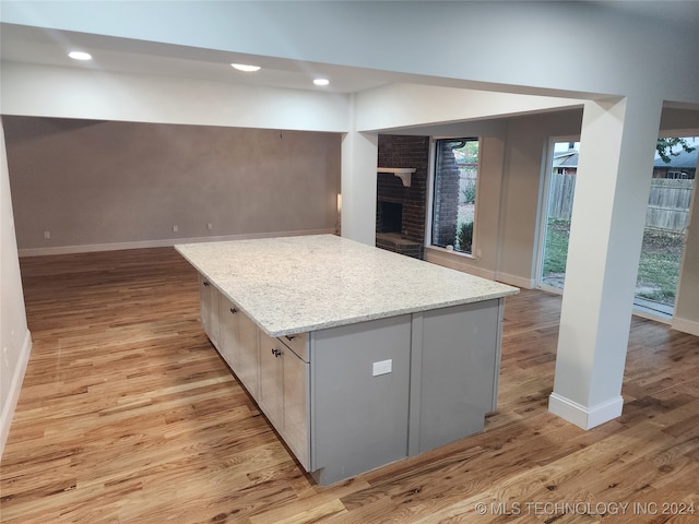 kitchen with a brick fireplace, light stone countertops, light wood-type flooring, and a kitchen island