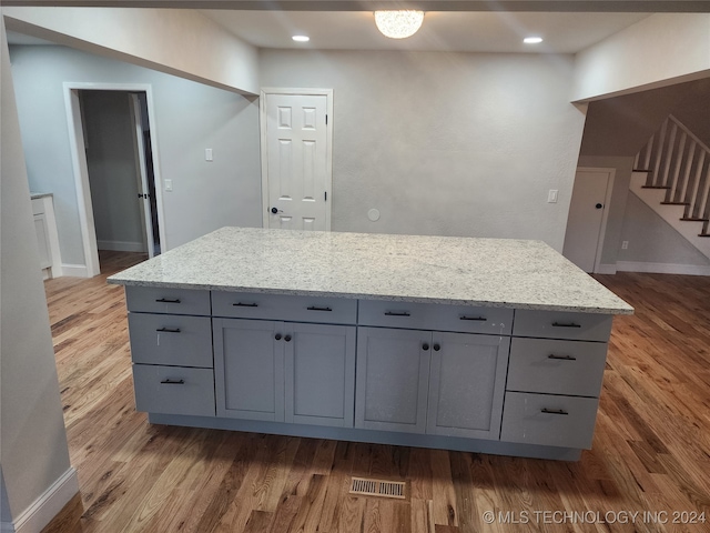 kitchen with gray cabinets, light stone counters, a center island, and dark hardwood / wood-style flooring