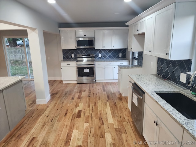 kitchen with appliances with stainless steel finishes, white cabinets, backsplash, light stone countertops, and light wood-type flooring