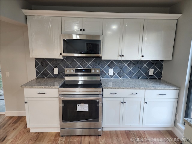 kitchen with stainless steel appliances, white cabinets, light hardwood / wood-style floors, and backsplash