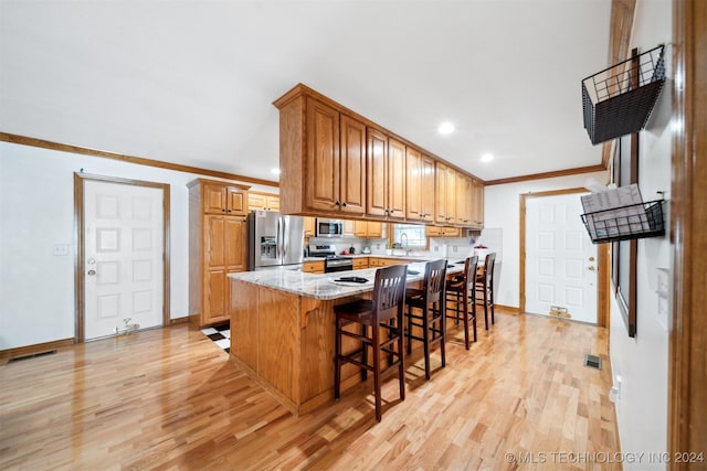 kitchen featuring a kitchen breakfast bar, light stone counters, a kitchen island, stainless steel appliances, and light hardwood / wood-style flooring