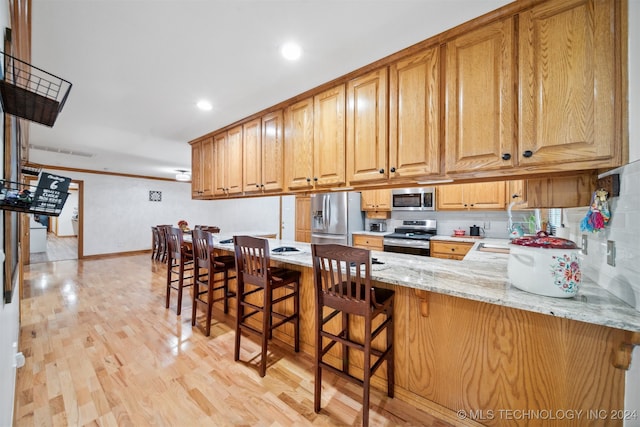 kitchen featuring a breakfast bar, kitchen peninsula, light hardwood / wood-style flooring, stainless steel appliances, and light stone countertops