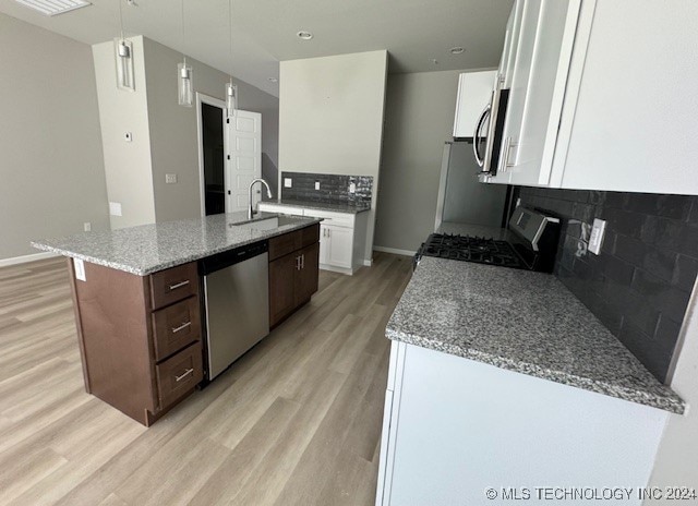 kitchen with appliances with stainless steel finishes, light wood-type flooring, white cabinetry, and light stone countertops