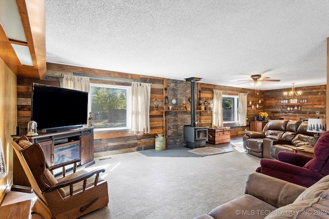 carpeted living room featuring ceiling fan, wood walls, a textured ceiling, and a wood stove