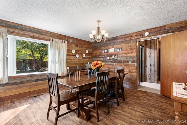 dining area with dark hardwood / wood-style flooring, a chandelier, a textured ceiling, and wood walls