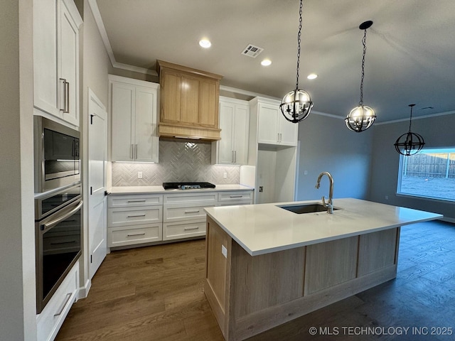 kitchen with built in microwave, oven, a kitchen island with sink, and white cabinets