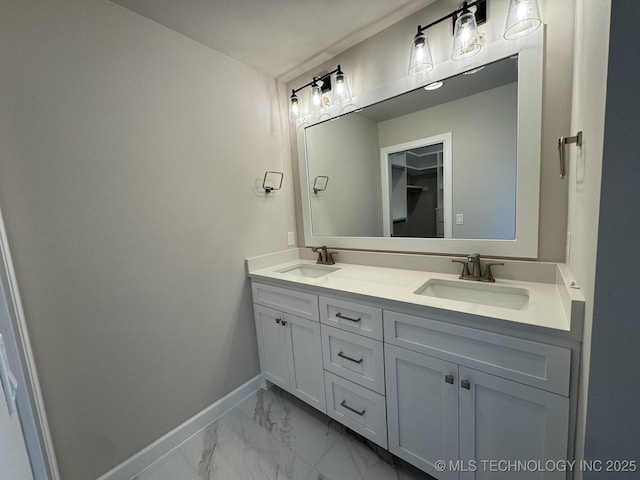 bathroom featuring double vanity, marble finish floor, baseboards, and a sink