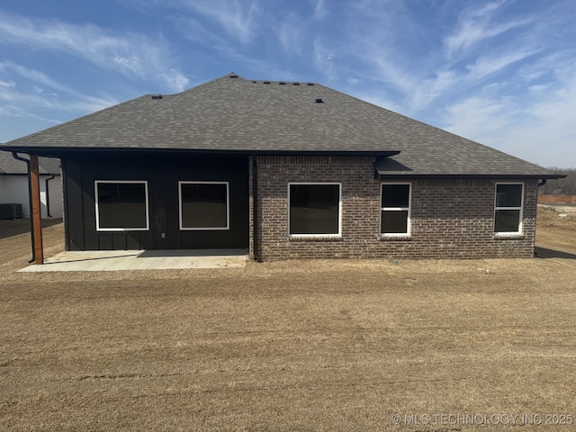 back of house featuring a patio, cooling unit, brick siding, roof with shingles, and board and batten siding