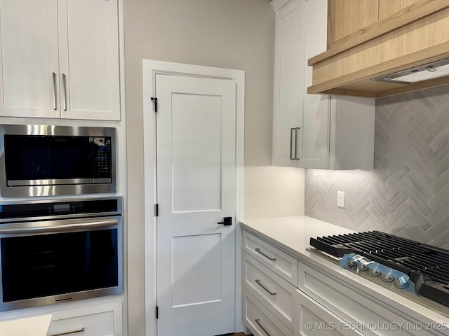 kitchen featuring tasteful backsplash, white cabinets, wall chimney exhaust hood, appliances with stainless steel finishes, and light countertops