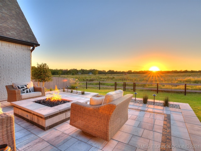 patio terrace at dusk featuring a lawn, a rural view, and an outdoor living space with a fire pit