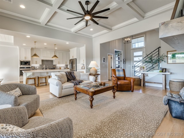 living room with coffered ceiling, ceiling fan with notable chandelier, light hardwood / wood-style flooring, and beam ceiling