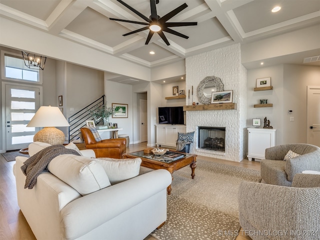 living room featuring coffered ceiling, ceiling fan with notable chandelier, a fireplace, beamed ceiling, and wood-type flooring