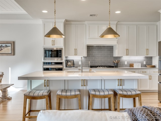 kitchen featuring an island with sink, appliances with stainless steel finishes, light wood-type flooring, and white cabinetry