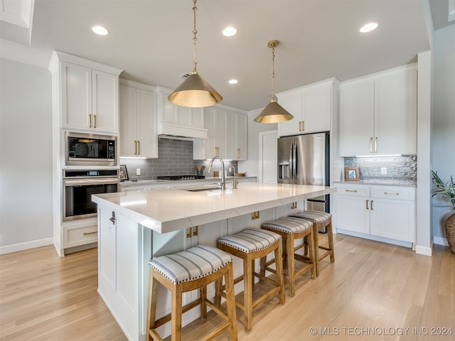 kitchen with white cabinets, sink, a center island with sink, appliances with stainless steel finishes, and light wood-type flooring