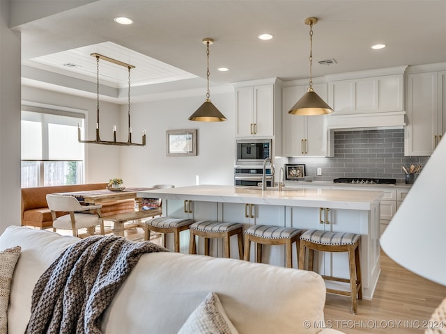 kitchen with decorative light fixtures, light hardwood / wood-style flooring, white cabinetry, stainless steel appliances, and a tray ceiling