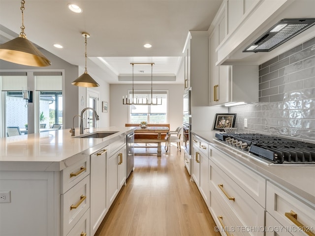 kitchen featuring hanging light fixtures, white cabinetry, a raised ceiling, a center island with sink, and sink