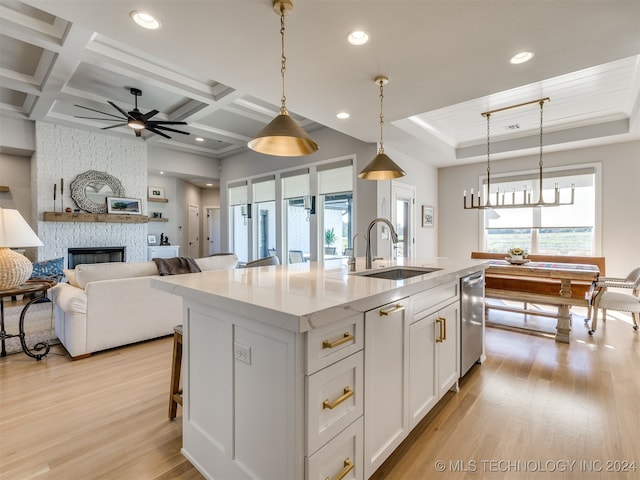 kitchen featuring white cabinets, hanging light fixtures, sink, a stone fireplace, and a center island with sink