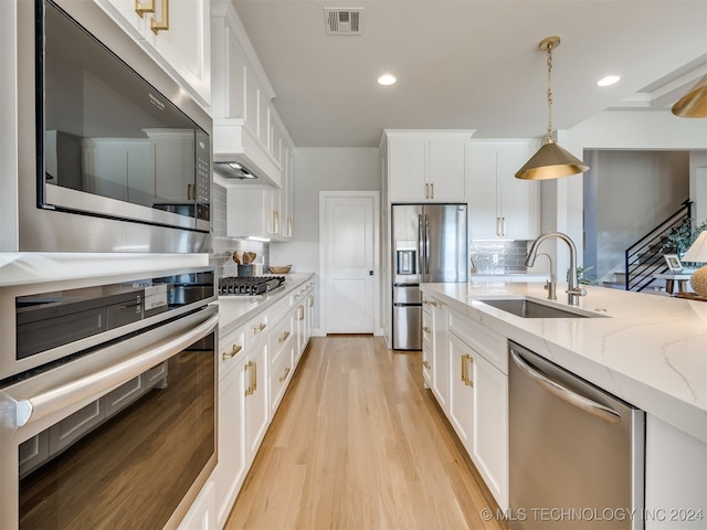 kitchen featuring white cabinetry, pendant lighting, stainless steel appliances, light wood-type flooring, and sink