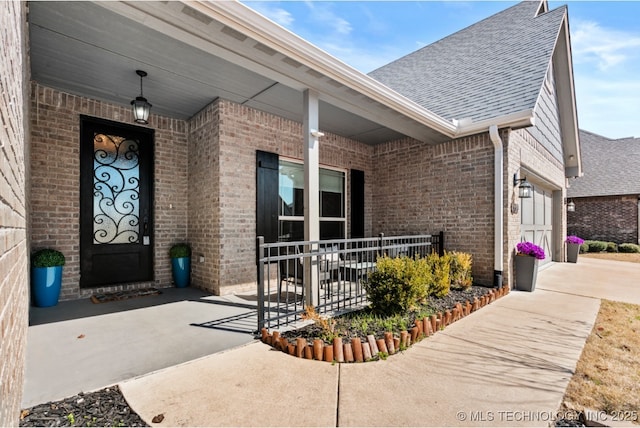 doorway to property with concrete driveway, a porch, brick siding, and roof with shingles