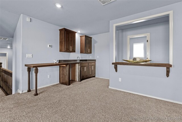 kitchen featuring visible vents, light carpet, a sink, baseboards, and dark brown cabinets