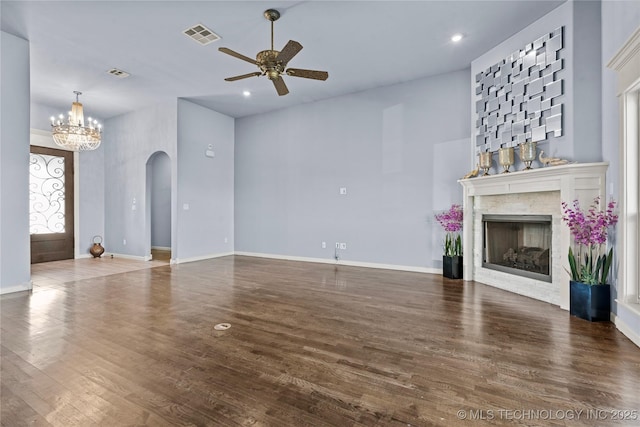 unfurnished living room with wood finished floors, baseboards, a fireplace, arched walkways, and ceiling fan with notable chandelier