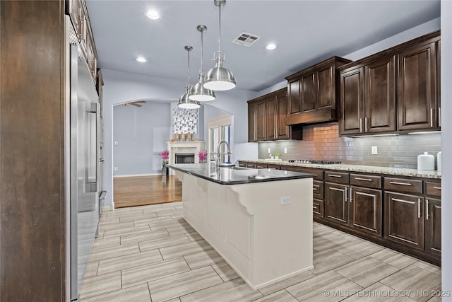 kitchen with visible vents, a sink, stainless steel gas stovetop, tasteful backsplash, and a large fireplace