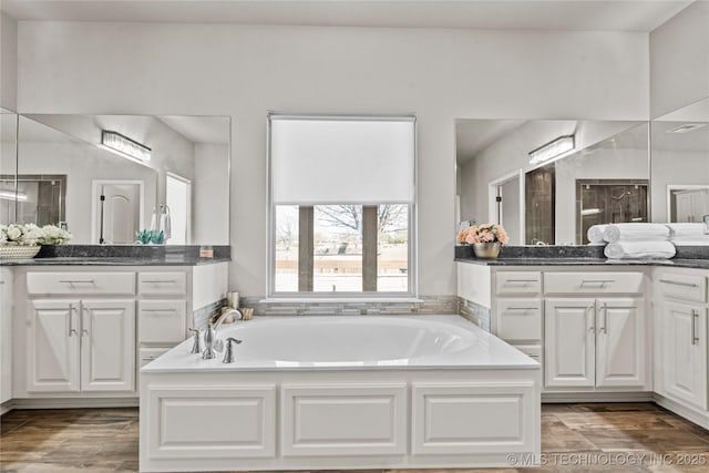 full bathroom with a garden tub, two vanities, and wood finished floors