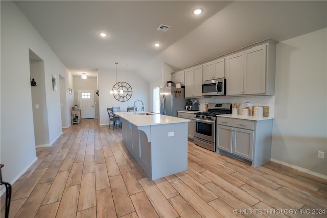 kitchen featuring vaulted ceiling, sink, an inviting chandelier, a kitchen island with sink, and stainless steel appliances